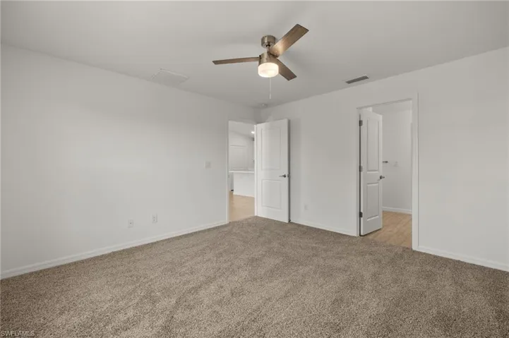 Unfurnished bedroom with baseboards, ceiling fan, visible vents, and light colored carpet