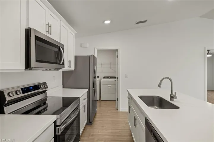Kitchen featuring stainless steel appliances, a sink, light countertops, and white cabinetry