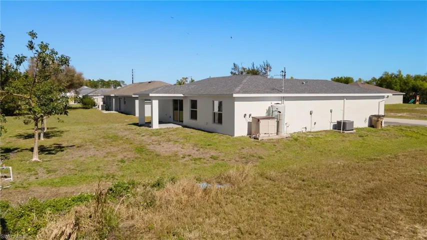 Back of property with central AC, a lawn, and stucco siding