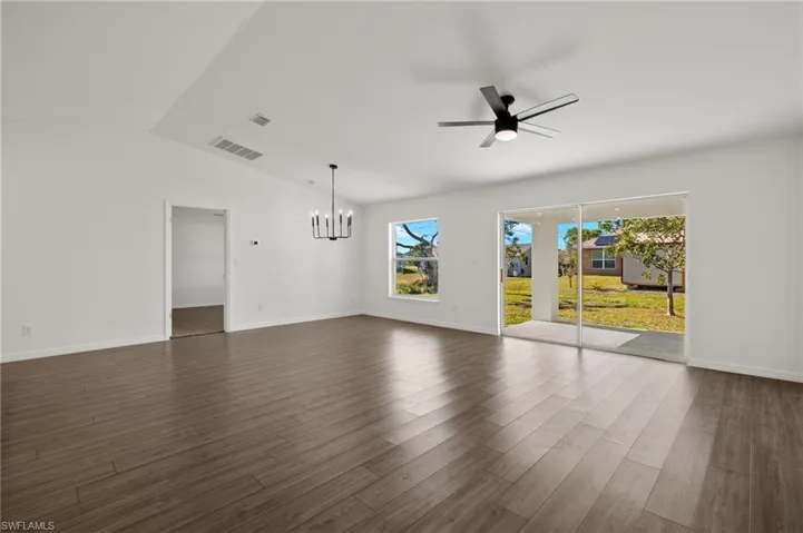 Unfurnished living room featuring baseboards, visible vents, dark wood finished floors, vaulted ceiling, and ceiling fan with notable chandelier