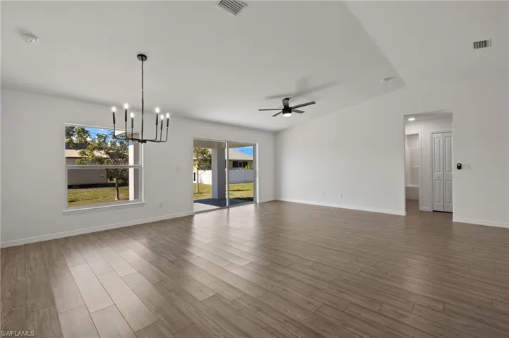Spare room featuring baseboards, visible vents, wood finished floors, and ceiling fan with notable chandelier