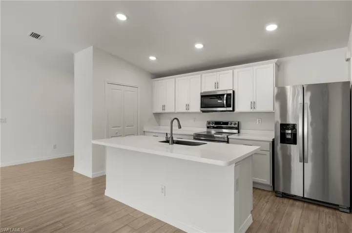Kitchen with a kitchen island with sink, appliances with stainless steel finishes, light countertops, and a sink