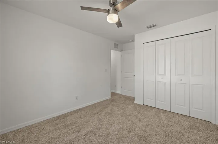 Unfurnished bedroom featuring light colored carpet, a ceiling fan, baseboards, visible vents, and a closet