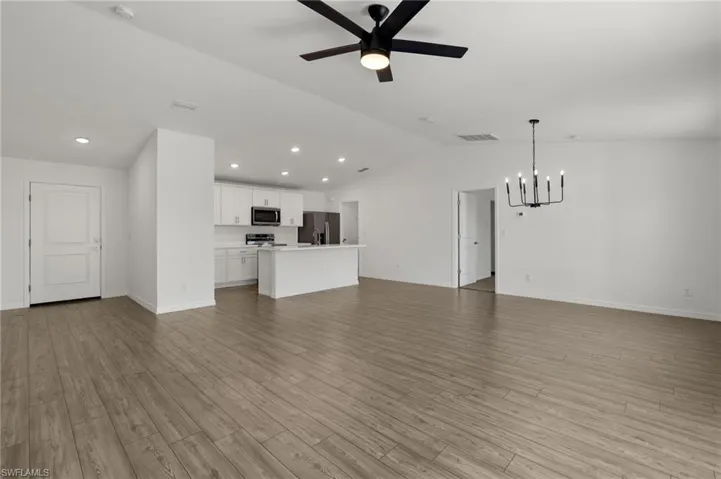 Unfurnished living room featuring lofted ceiling, visible vents, light wood-style flooring, baseboards, and ceiling fan with notable chandelier
