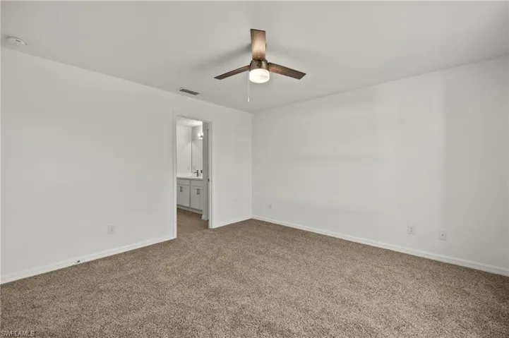 Unfurnished bedroom featuring visible vents, a ceiling fan, carpet flooring, ensuite bath, and baseboards