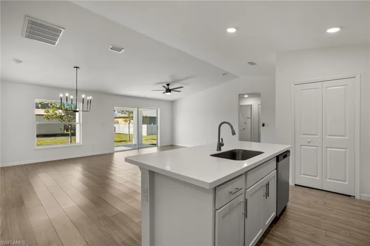 Kitchen with light countertops, visible vents, open floor plan, a sink, and an island with sink