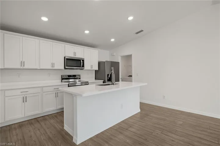 Kitchen featuring stainless steel appliances, a sink, white cabinetry, light countertops, and an island with sink
