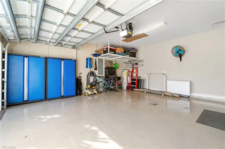Garage includes overhead storage, cabinets, vacuum, fan, and refrigerator