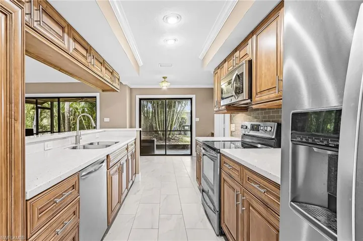Galley kitchen featuring wood cabinetry, light-toned countertops, and stainless steel appliances