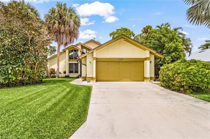 Two-car garage, concrete driveway, mature landscaping, and a multi-level roofline