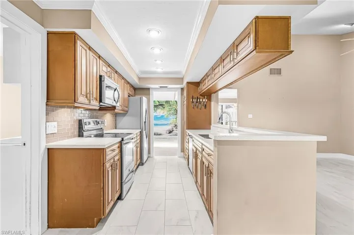 Galley kitchen with wood cabinetry, stainless steel appliances, light-toned countertops, tile flooring, and recessed lighting