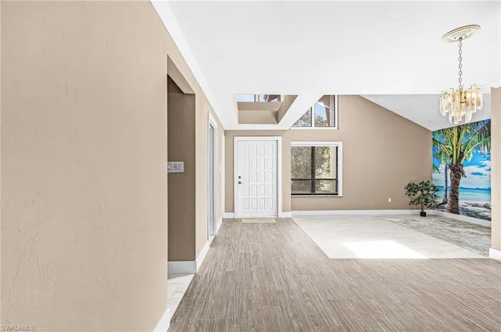 Wood-finish flooring, white paneled entry door, transom windows, vaulted ceiling, and a decorative chandelier