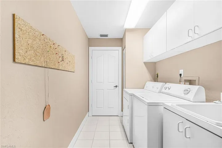 Laundry area with white cabinetry, a utility sink, and tile flooring