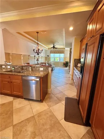 Kitchen featuring brown cabinetry, ornamental molding, a tray ceiling, dishwasher, and dark stone counters