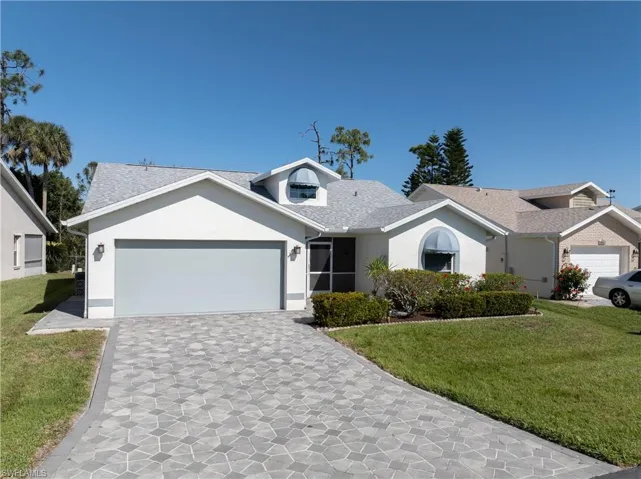 Ranch-style home featuring an attached garage, a shingled roof, stucco siding, a front lawn, and decorative driveway