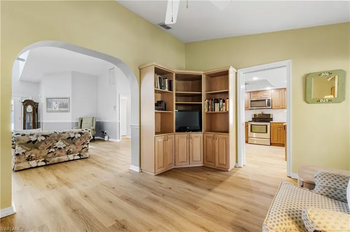 Living area featuring light wood finished floors, visible vents, baseboards, ceiling fan, and arched walkways