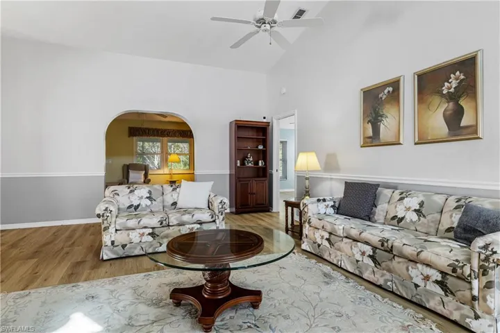 Living room with visible vents, a ceiling fan, wood finished floors, arched walkways, and vaulted ceiling
