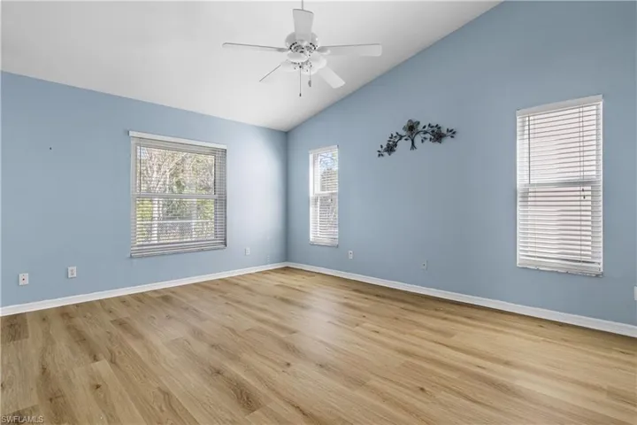 Empty room featuring light wood finished floors, baseboards, ceiling fan, and vaulted ceiling
