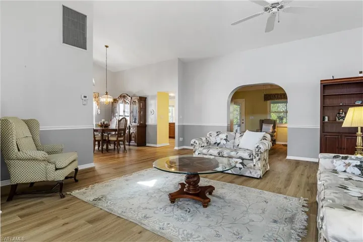 Living area featuring visible vents, ceiling fan with notable chandelier, arched walkways, light wood-style floors, and baseboards