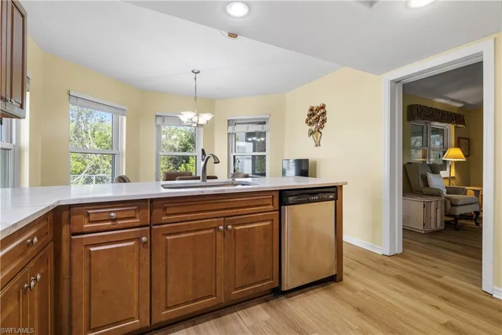 Kitchen featuring decorative light fixtures, stainless steel dishwasher, light wood-style floors, brown cabinetry, and a sink