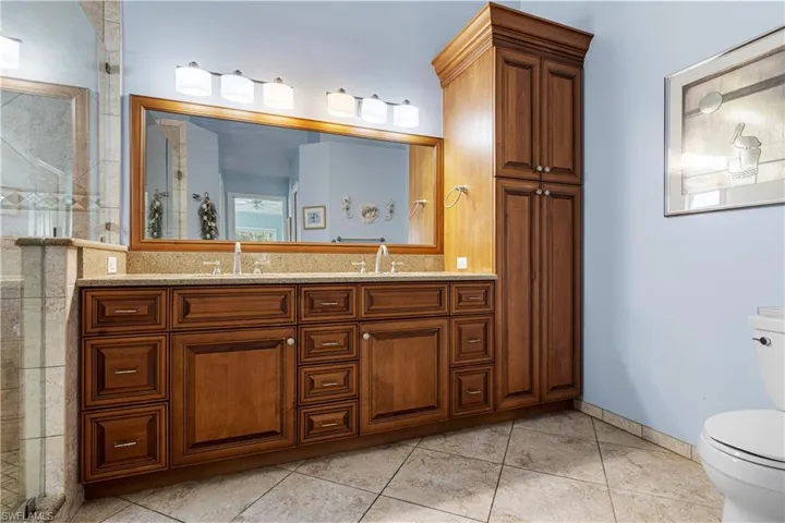 Full bath with double vanity, tiled shower, toilet, and a sink