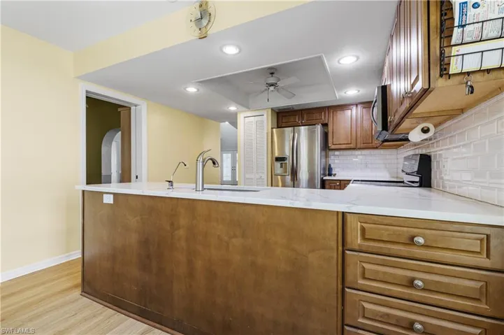 Kitchen with a ceiling fan, brown cabinetry, light wood-style flooring, appliances with stainless steel finishes, and tasteful backsplash