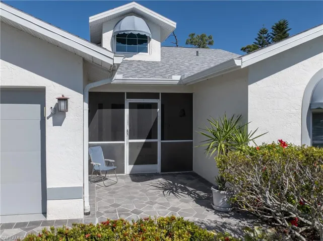 Entrance to property featuring a patio area, roof with shingles, and stucco siding