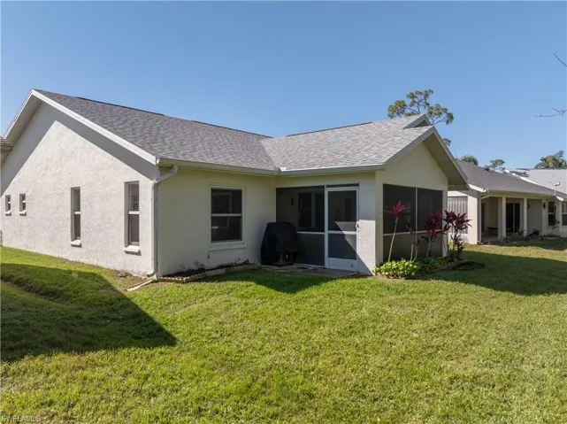 Rear view of house with stucco siding, a shingled roof, and a yard