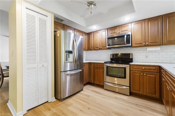 Kitchen with light wood-type flooring, a raised ceiling, backsplash, and appliances with stainless steel finishes