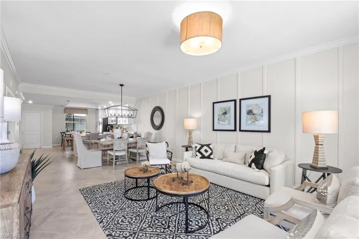 Living room with a decorative wall, a notable chandelier, crown molding, and light tile patterned flooring