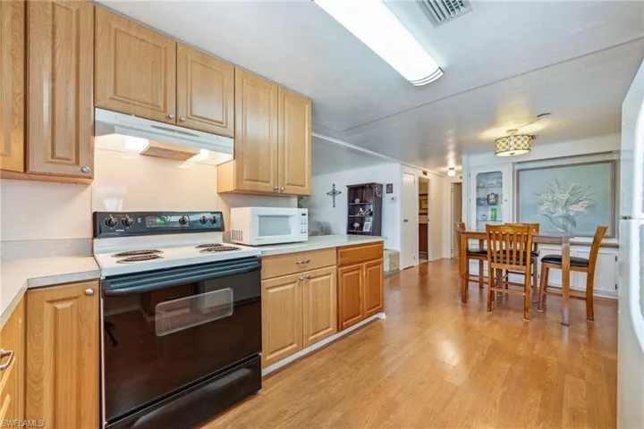 Kitchen with white appliances, light countertops, under cabinet range hood, and light wood-style floors