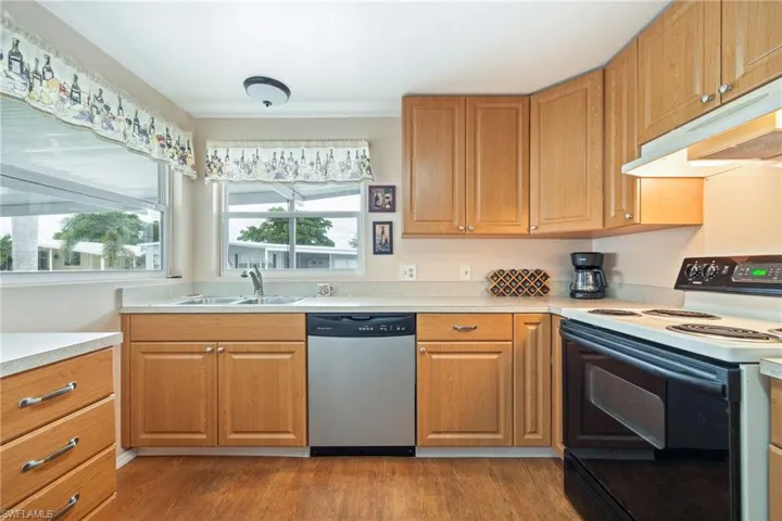 Kitchen with electric stove, light countertops, dishwasher, dark wood finished floors, and under cabinet range hood