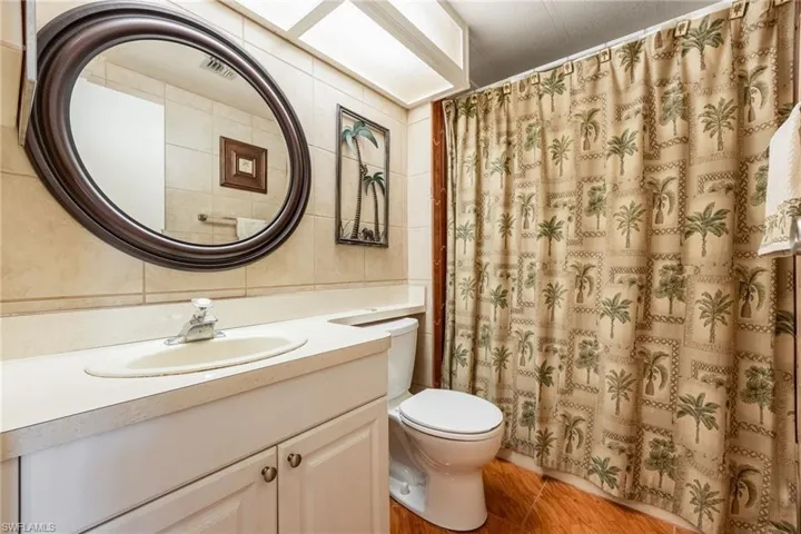 Full bath with tile walls, vanity, light wood-type flooring, and a shower with shower curtain