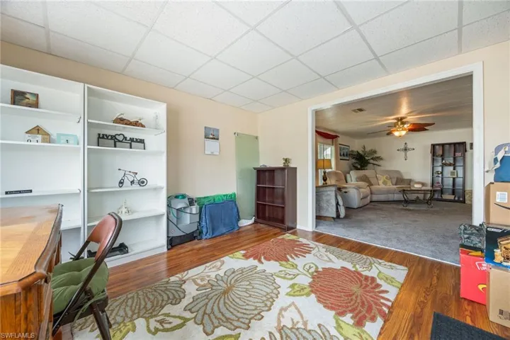 Living area with wood finished floors, ceiling fan, a desk, and a paneled ceiling
