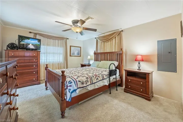 Bedroom with electric panel, light colored carpet, and ceiling fan
