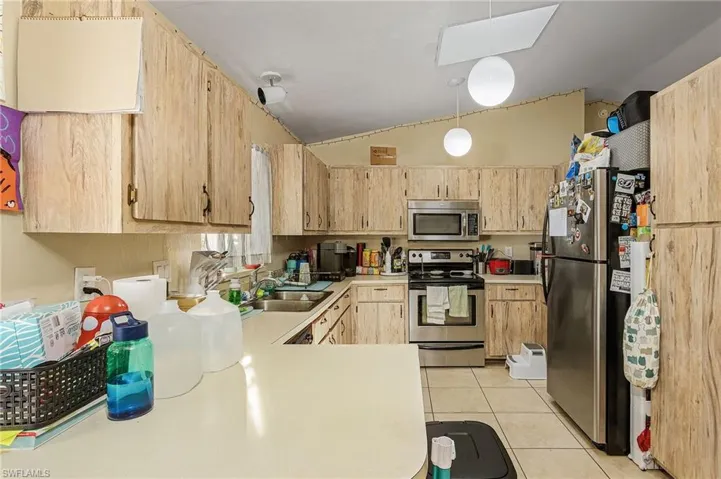Kitchen with light brown cabinets, sink, stainless steel appliances, lofted ceiling, and light tile patterned flooring