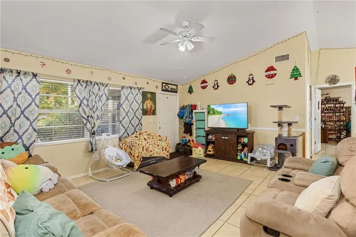 Living room with ceiling fan, light tile patterned flooring, and vaulted ceiling