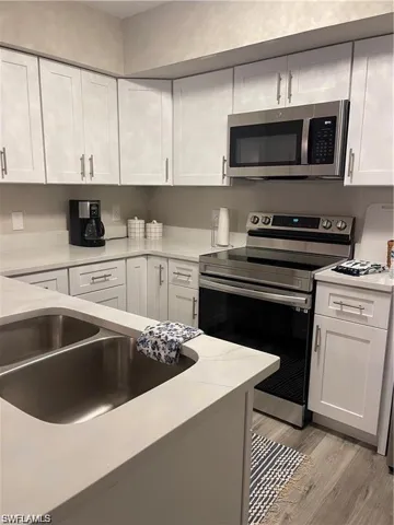 Kitchen with appliances with stainless steel finishes, white cabinets, light wood-style floors, and light stone countertops
