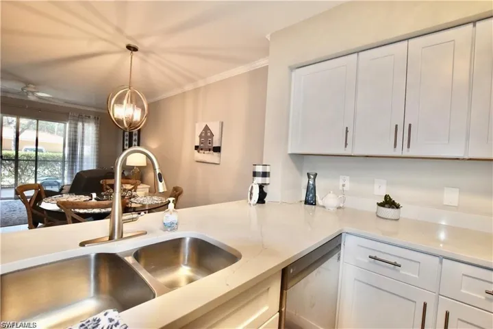 Kitchen featuring white cabinets, stainless steel dishwasher, open floor plan, ornamental molding, and light stone counters