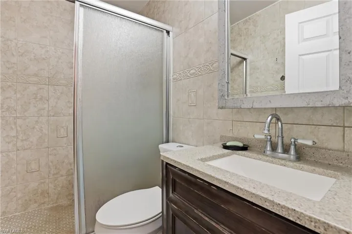 Full bath with a stall shower, vanity, tile walls, and tasteful backsplash