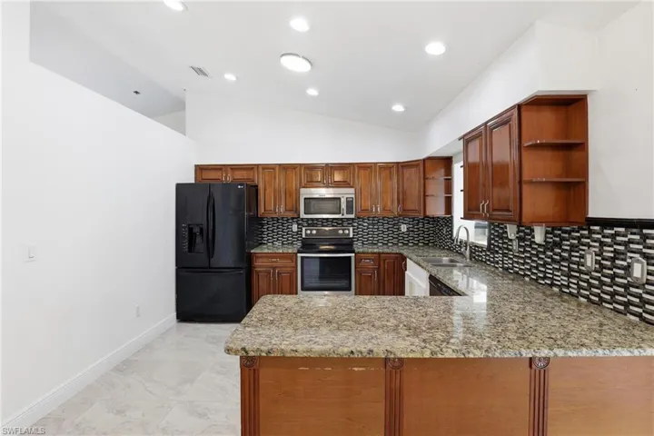 Kitchen featuring open shelves, lofted ceiling, stainless steel appliances, light stone countertops, and a peninsula