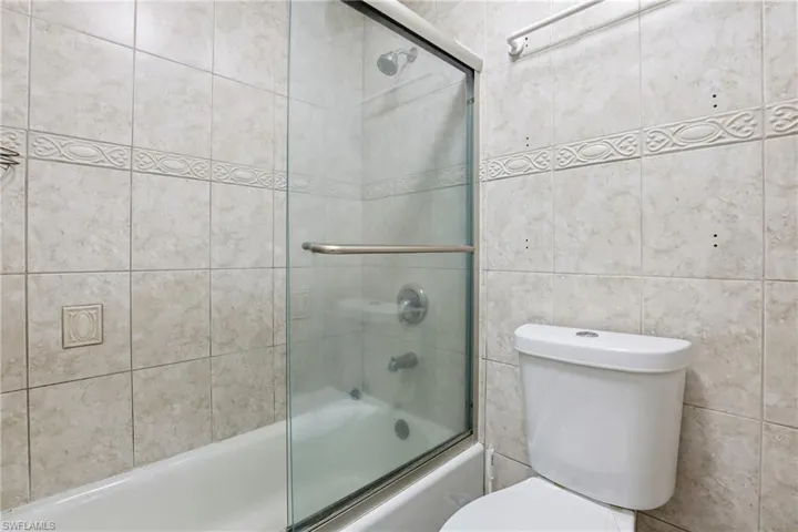 Full bath featuring combined bath / shower with glass door and tile walls