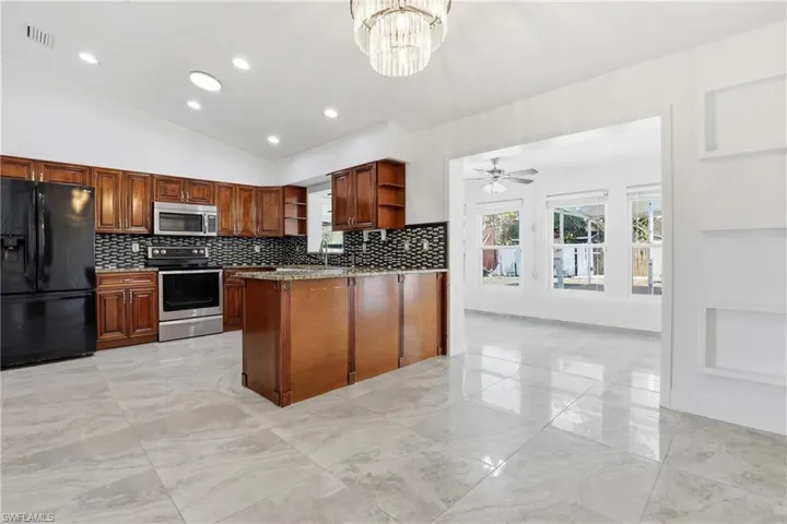 Kitchen with open shelves, stainless steel appliances, lofted ceiling, a peninsula, and light stone counters