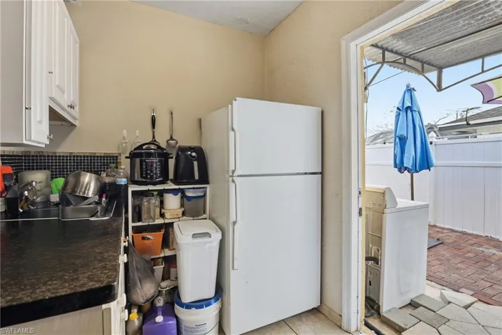 Kitchen with freestanding refrigerator, dark countertops, washer / clothes dryer, white cabinets, and brick floors