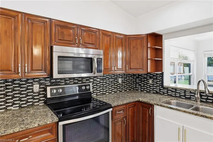 Kitchen featuring stainless steel appliances, dark stone counters, open shelves, vaulted ceiling, and wood finish cabinets