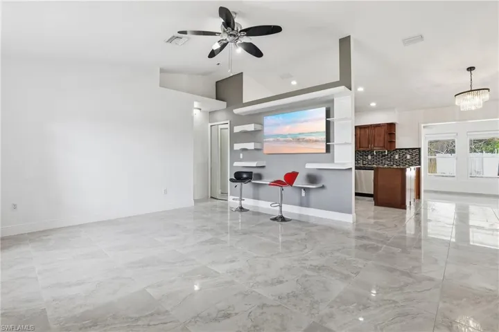 Unfurnished living room with ceiling fan, suspended lighting, light marble finish floors, and vaulted ceiling