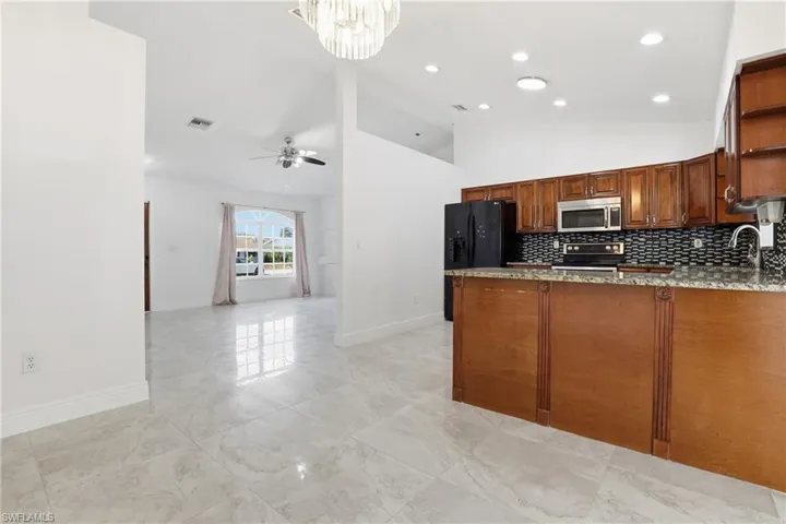 Kitchen with light stone countertops, black appliances, a peninsula, open shelves, and vaulted ceiling