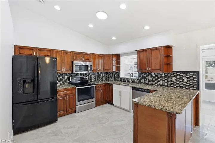 Kitchen featuring lofted ceiling, open shelves, light stone counters, stainless steel appliances, and wood finish cabinets