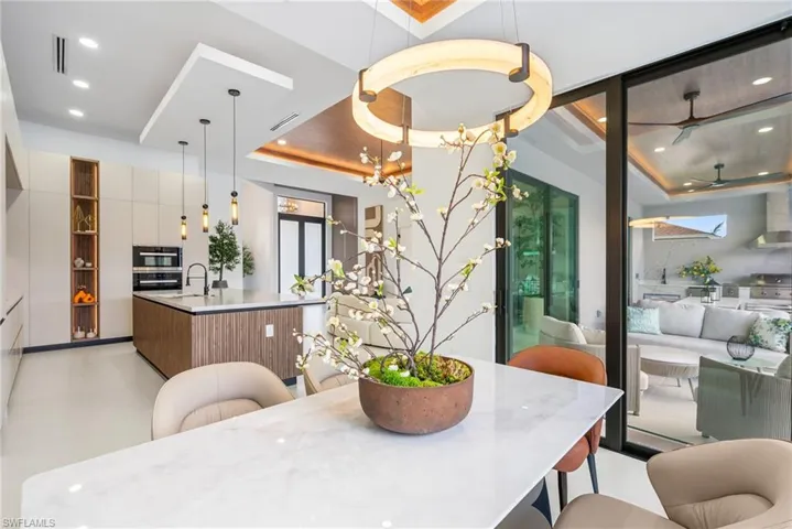 Open-concept kitchen and dining area featuring a large center island with integrated sink, sleek cabinetry with open shelving, and built-in appliances