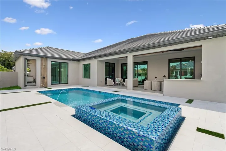 Outdoor living space featuring a rectangular pool with an integrated spa, mosaic tile detailing, and a water feature